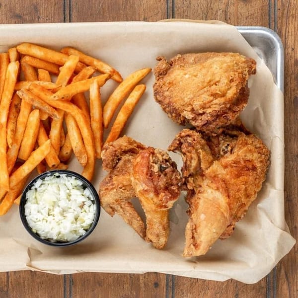 Crispy fried chicken pieces, golden french fries, and a side of coleslaw on a metal tray.